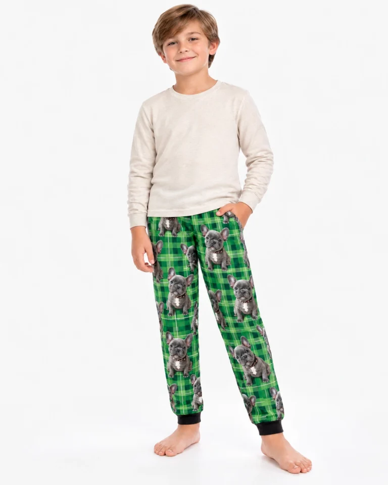 Boy wearing kids pajama pants printed with grey French bulldog faces on green plaid