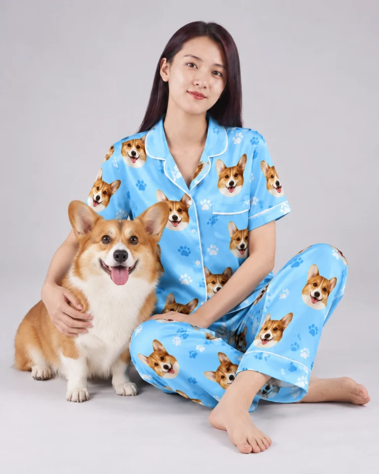 Woman in pajamas printed with dog faces, cuddling her corgi — MyDogPics